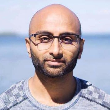 A bald man with a beard wearing glasses and a striped shirt, with a serene water background.