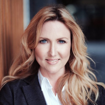 Portrait of a confident professional woman with long blonde hair and a business jacket, featuring a soft smile and poised demeanor.