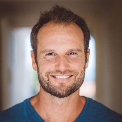 A smiling person with stubble wearing a blue t-shirt, radiating a friendly and approachable demeanor.