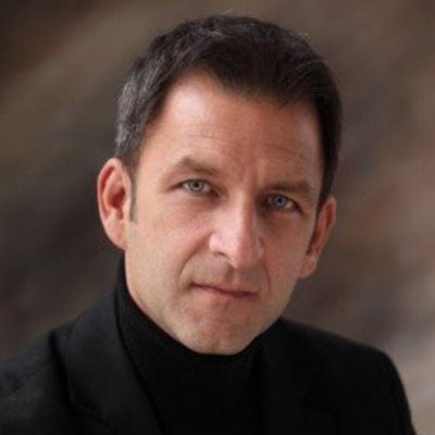 A portrait of a man with short hair wearing a black turtleneck, giving a confident and direct gaze to the camera.