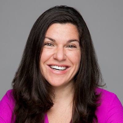 Professional woman with a friendly smile wearing a vibrant pink blouse against a grey background.