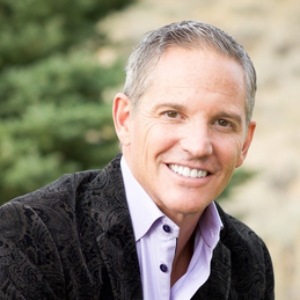 Confident smile from a man in a stylish patterned jacket and a sharp pink shirt.
