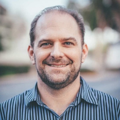 A smiling man with facial hair and a striped shirt posing for a portrait outdoors.