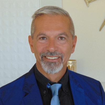 A smiling man with a neatly trimmed beard and mustache, wearing a dark suit with a blue shirt and matching tie.