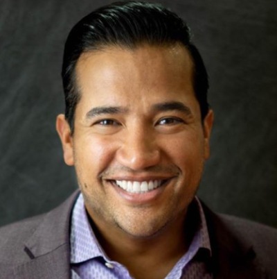A smiling person wearing a business casual attire with a blazer and a button-up shirt.