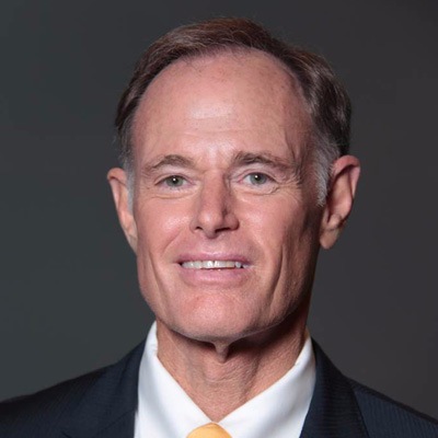 A professional headshot of a smiling man wearing a suit with a tie.