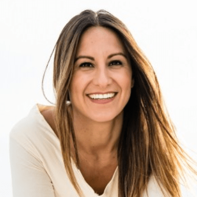 A smiling woman with long, straight brown hair against a bright white background. she is wearing a light-colored top and exudes a cheerful and confident demeanor.
