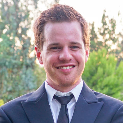 A smiling man dressed in a formal suit with a black tie, exuding confidence and cheerfulness.