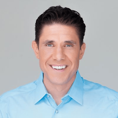 A smiling man with neatly combed hair, wearing a light blue button-up shirt against a gray background.