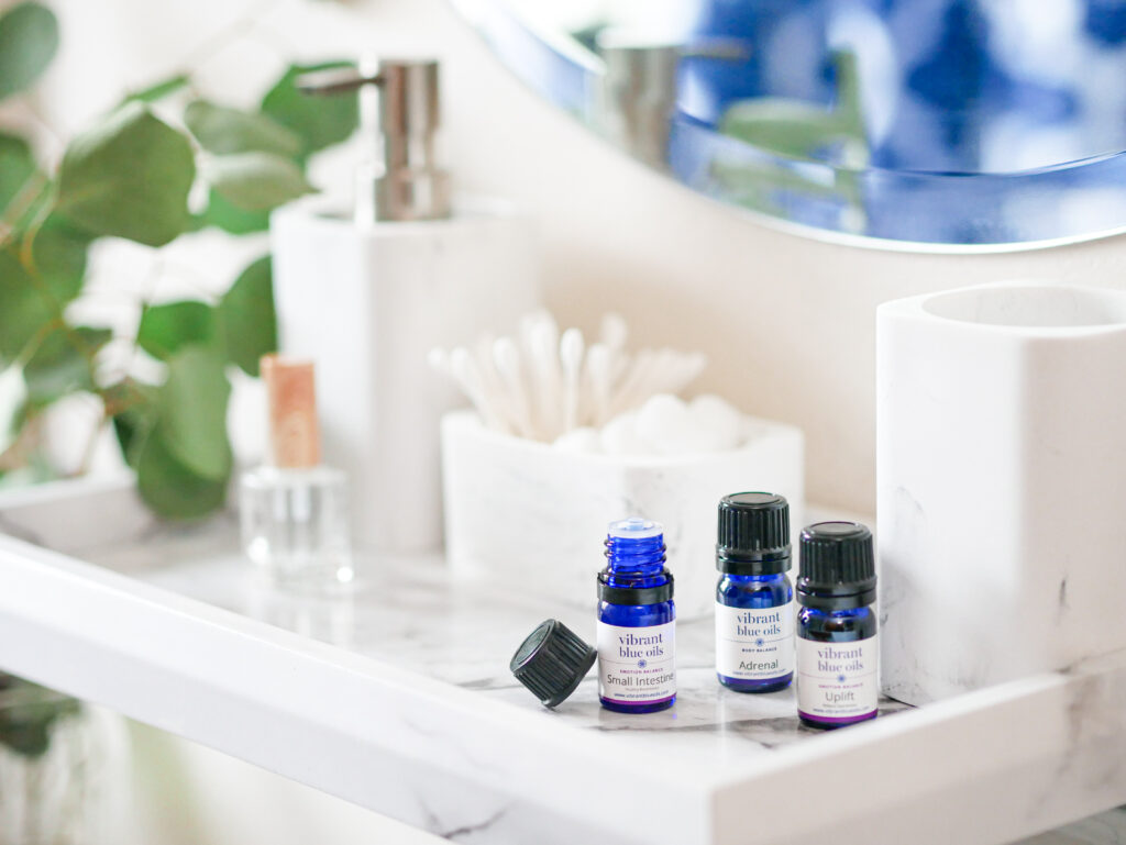 Elegant bathroom shelf with a serene setup of wellness products: essential oil bottles, marble accessories, and green foliage, reflecting a tranquil self-care atmosphere.