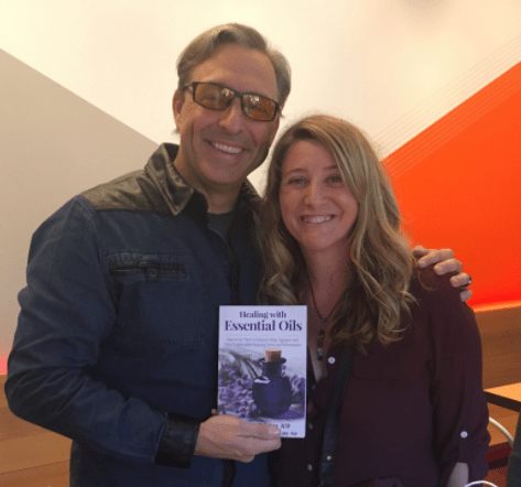 Two smiling individuals posing for a photo while holding a book titled "healing with essential oils.